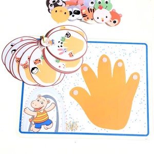 May include: A colorful educational game for kids featuring a hand with five fingers and various animal faces. The game includes a set of cards with different animal faces and a large hand with five fingers. The game is designed to help children learn about animals and their names.