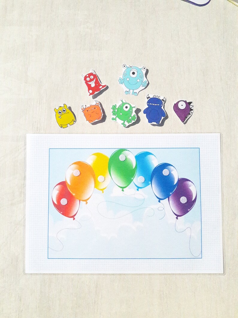 May include: A rainbow-colored balloon arch with white polka dots, a blue background, and white clouds. There are eight colorful monster stickers on a white background above the balloon arch.