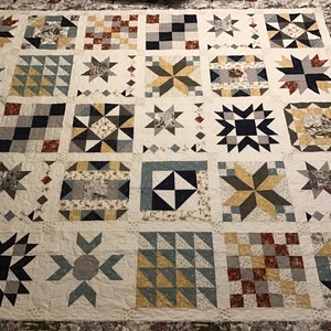 May include: A quilt with a patchwork design featuring various geometric patterns in shades of blue, gray, white, and yellow. The quilt is made up of individual squares, each with a different pattern.