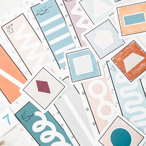 Op de afbeelding: Een set kleurrijke kaarten met geometrische vormen en hun namen. De kaarten liggen op een wit oppervlak. De vormen omvatten een vierkant, een rechthoek, een trapezium, een parallellogram, een ruit, een vijfhoek en een halve maan.