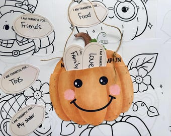 May include: A paper pumpkin with a smiling face and the words "I am thankful for..." on several attached tags. The tags say "Friends", "Food", "Toys", "My sister", "Family", and "Love". The pumpkin is orange with pink cheeks.