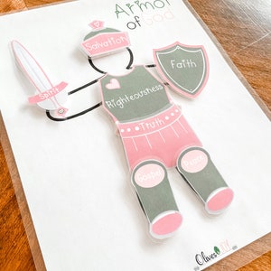 May include: A pink and green felt play set for children featuring a knight in armor with the words "Armor of God" at the top. The knight's armor pieces are labeled with words like "Salvation", "Faith", "Righteousness", "Truth", "Gospel", "Peace", and "Spirit".