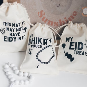 May include: Three white cotton drawstring bags with black text. The bags are labelled "This may not have Eidy in it.", "My Dhikr Pouch" and "My Eid Treats".