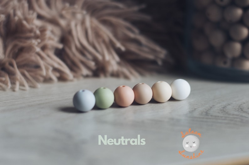 May include: A row of seven round wooden beads in various neutral colors, including light blue, green, peach, beige, and white. The beads are arranged in a line on a light wood surface. The text "Neutrals" is written below the beads.