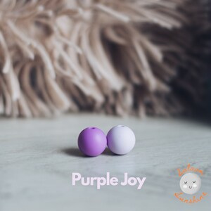 May include: Two silicone beads, one purple and one light purple, on a white surface. The text "Purple Joy" is printed below the beads.