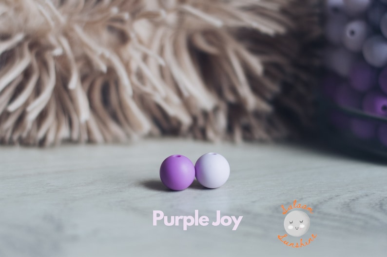 May include: Two silicone beads, one purple and one light purple, on a white surface. The text "Purple Joy" is printed below the beads.