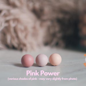 May include: Three round beads in various shades of pink. The beads are arranged in a row on a white surface. The text "Pink Power" is written below the beads. The text "(various shades of pink - may vary slightly from photo)" is written below the text "Pink Power".