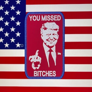 May include: An embroidered patch in red, white and blue with a white image of a man wearing a white shirt and tie, giving a thumbs up. The text "YOU MISSED" is above the image and the text "BITCHES" is below the image.
