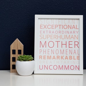 Può includere: Stampa incorniciata bianca con la parola "MAMMA" in grandi lettere rosa circondata da parole come "eccezionale", "sovrumano", "notevole" e "insolito" in un gradiente di rosa e bianco.