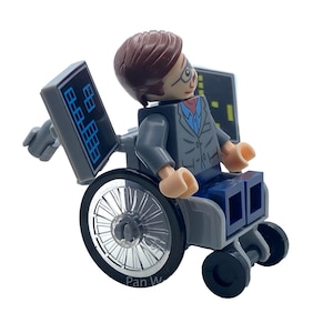 May include: A Lego minifigure of a person in a wheelchair, wearing a gray suit, glasses, and a red tie. The wheelchair has large silver wheels and small black wheels. Two gray panels with blue and white graphics are attached to the chair.