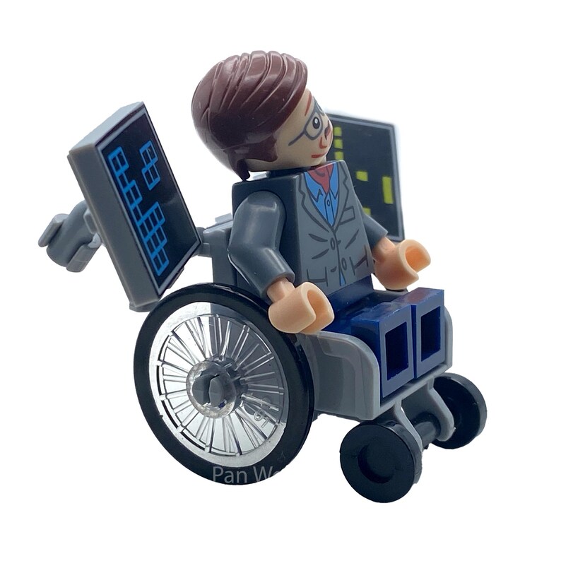 May include: A Lego minifigure of a person in a wheelchair, wearing a gray suit, glasses, and a red tie. The wheelchair has large silver wheels and small black wheels. Two gray panels with blue and white graphics are attached to the chair.