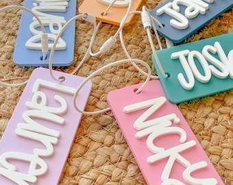 May include: Six colorful luggage tags with white lettering. The names on the tags are Chloe, Daniel, James, Josie, Laura, and Nicky.