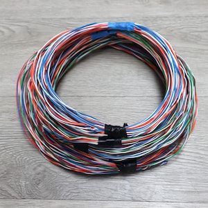 May include: A bundle of colorful electrical wires, including red, blue, green, and white, is coiled into a circular shape. The wires are secured with blue tape and black tape. The image is taken from a high angle.