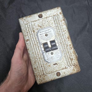 May include: A vintage Westinghouse Multi-Breaker electrical panel with a weathered, rusted metallic finish. The rectangular unit features two black toggle switches, printed technical specifications, and instructions for resetting the circuit breakers.