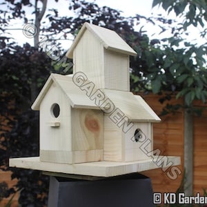 May include: A wooden birdhouse with a multi-level design. The birdhouse has a rectangular base and a series of gabled roofs. The birdhouse has a natural wood color and features circular entry holes. The text "KD Garden Plans" is visible.