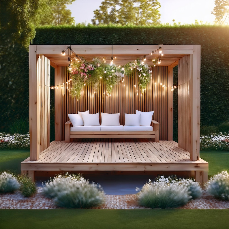May include: A wooden outdoor structure with a built-in bench and string lights. The structure features a slatted wooden back and a wooden deck. White cushions adorn the bench, and hanging plants and flowers add a touch of nature. The scene is set in a garden.