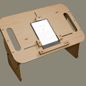 May include: A wooden stand with a built-in book holder, designed to hold an e-reader. The stand is made of light wood and has a natural finish. The e-reader is a Kindle and is displaying the text "CHAPTER 1".