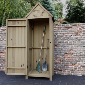 Può includere: Un capanno di legno con una porta aperta. Il capanno è dipinto di un colore marrone chiaro e ha una piccola finestra sul davanti. Ci sono due attrezzi da giardino all'interno del capanno.
