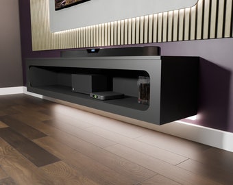 May include: A black floating shelf with rounded edges, mounted on a purple wall. The shelf has two compartments, one with a black speaker and the other with a black media player. The shelf is illuminated with white LED lights.