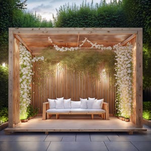May include: A wooden pergola with a slatted back and ceiling, adorned with white flowers and greenery. A wooden bench with white cushions sits inside. The structure is surrounded by lush greenery and small potted plants, creating a serene outdoor space.