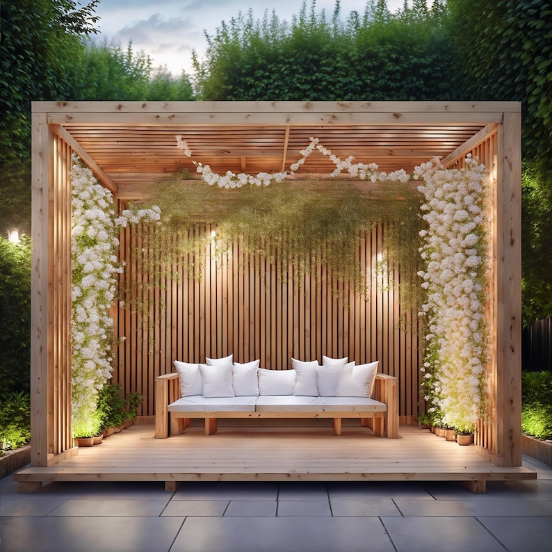 May include: A wooden pergola with a slatted back and ceiling, adorned with white flowers and greenery. A wooden bench with white cushions sits inside. The structure is surrounded by lush greenery and small potted plants, creating a serene outdoor space.