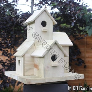 May include: A multi-compartment wooden birdhouse with a natural finish. The birdhouse has multiple levels, each with a circular entrance hole. The design includes a small perch below each hole. The text "KDM GARDEN PLANS" and "KD Garden Products" are visible.