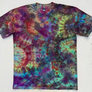 May include: A short-sleeved t-shirt with a tie-dye pattern in shades of purple, red, green, and blue. The shirt has a crew neck and a soft, textured appearance. The tie-dye design creates a swirling, colorful effect across the fabric.