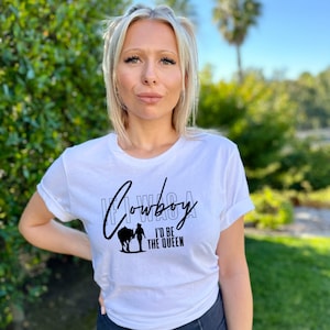 Peut inclure: T-shirt blanc avec un texte noir qui dit "If I Was A Cowboy I'd Be The Queen". Le texte est dans une police stylis&eacute;e et comprend une silhouette d'une femme &agrave; cheval.