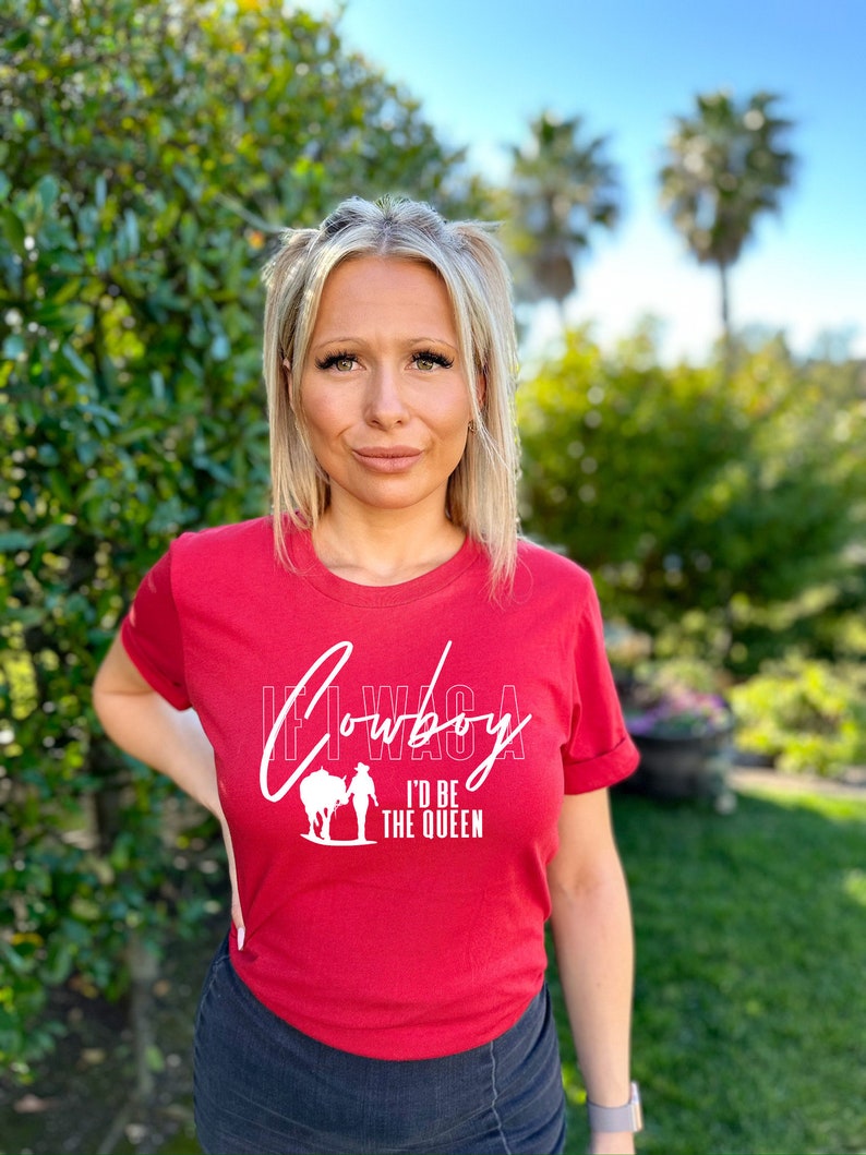 Peut inclure: T-shirt rouge avec un graphisme blanc qui dit "If I Was A Cowboy I'd Be The Queen" et une silhouette de femme &agrave; cheval.