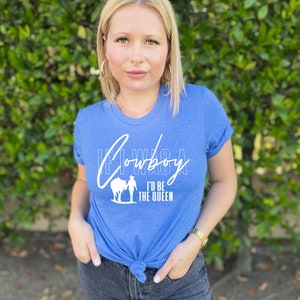 Peut inclure: Un t-shirt bleu avec un motif blanc qui dit "Si j'&eacute;tais un cowboy, je serais la reine".