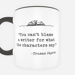 May include: White ceramic mug with a black handle and rim. The mug features a quote by Truman Capote: "You can't blame a writer for what the characters say." A line drawing of an open book is above the quote.