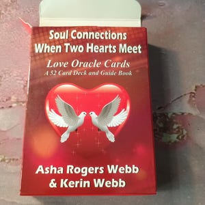 May include: A red box with a white border and a white heart with two white doves inside. The text on the box reads "Soul Connections When Two Hearts Meet Love Oracle Cards A 52 Card Deck and Guide Book Asha Rogers Webb & Kerin Webb".