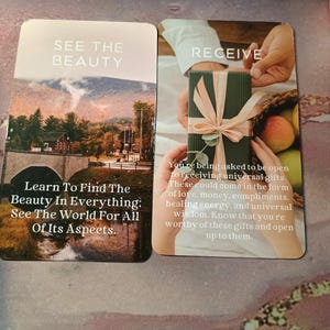 May include: Two cards with inspirational messages. The first card has a photo of a bridge and mountains with the text "See the Beauty. Learn to find the beauty in everything: See the world for all of its aspects." The second card has a photo of a hand receiving a wrapped gift with the text "Receive. You're being asked to be open to receiving universal gifts. These could come in the form of love, money, compliments, healing energy, and universal wisdom. Know that you're worthy of these gifts and open up to them."