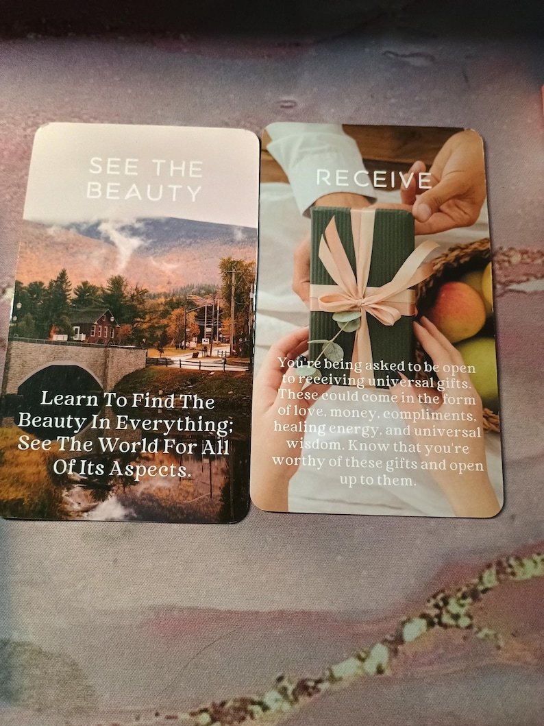 May include: Two cards with inspirational messages. The first card has a photo of a bridge and mountains with the text "See the Beauty. Learn to find the beauty in everything: See the world for all of its aspects." The second card has a photo of a hand receiving a wrapped gift with the text "Receive. You're being asked to be open to receiving universal gifts. These could come in the form of love, money, compliments, healing energy, and universal wisdom. Know that you're worthy of these gifts and open up to them."