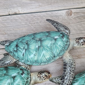 May include: Several decorative sea turtles with teal shells and detailed patterns. The turtles have textured skin and are arranged on a light wood-grain surface. The turtles are a decorative item.