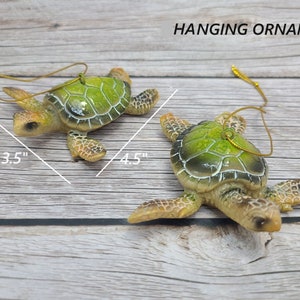 A beautifully crafted green sea turtle ornament made of glass, featuring lifelike details of the turtle's shell and flippers. The ornament showcases shades of vibrant green, with intricate patterns on its shell. Suspended by a silver thread