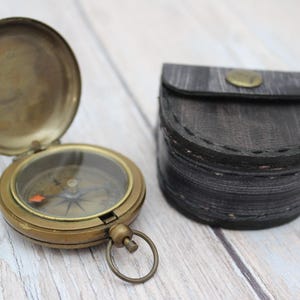 Vintage brass pocket compass with protective leather case on wooden background.