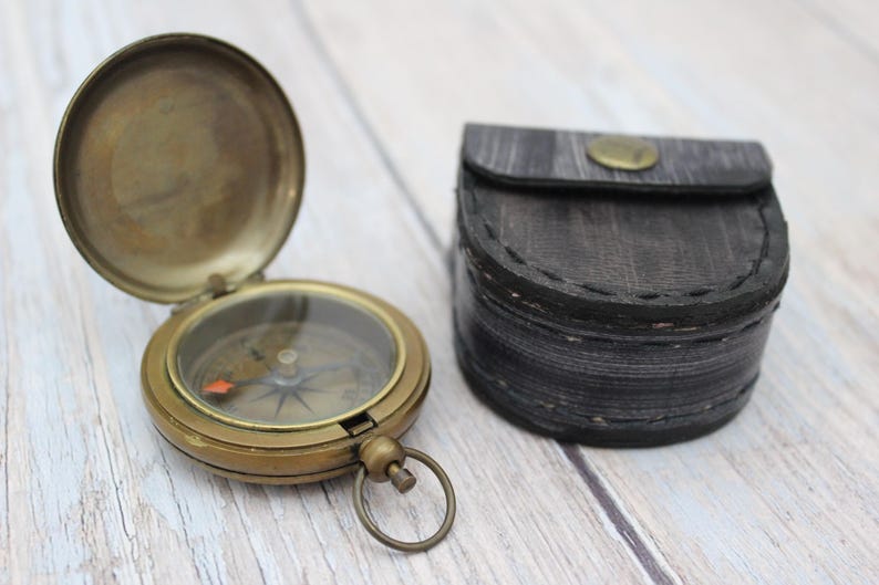 Vintage brass pocket compass with protective leather case on wooden background.
