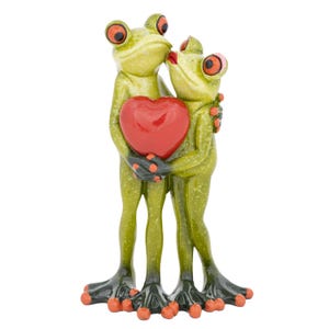May include: A whimsical figurine of two green frogs embracing and kissing, holding a red heart. The frogs have orange eyes and spots, with black feet and orange toes. A romantic decorative item.