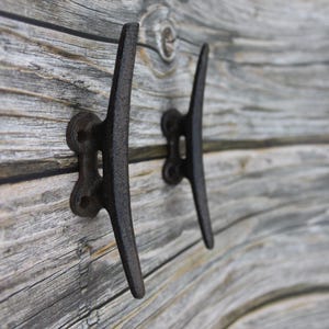 May include: Two black metal boat cleat hooks mounted on a weathered gray wood wall.
