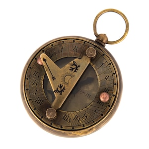 May include: Antique brass sundial with Roman numerals and a hinged gnomon. The sundial features a circular design with a ring for hanging. The gnomon has a sun and tree design. The sundial is a vintage item.