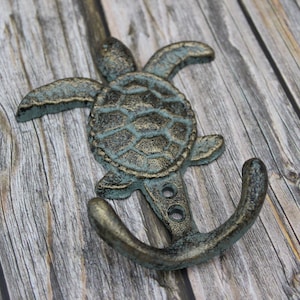 May include: A cast iron double hook with a sea turtle design. The hook is painted in a teal and gold finish.