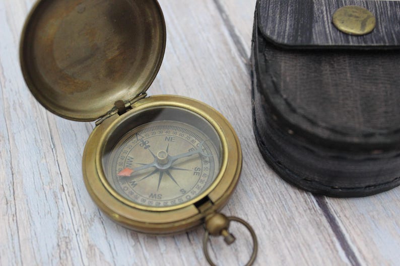Vintage brass pocket compass with protective leather case on wooden background
