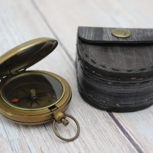 Vintage brass pocket compass with protective leather case on wooden background.