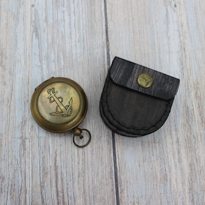 Vintage brass pocket compass with protective leather case on wooden background.