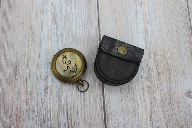 Vintage brass pocket compass with protective leather case on wooden background.