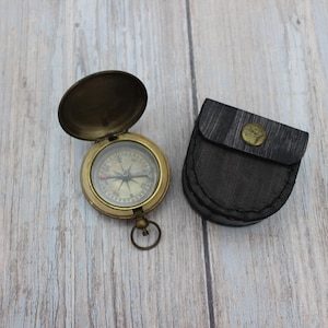 Vintage brass pocket compass with protective leather case on wooden background.