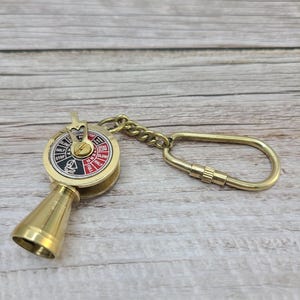 May include: A brass ship's wheel keychain with a red and white dial that reads "Full, Half, Slow, Stop, Astern, Full". The keychain has a brass ring and a brass hook.
