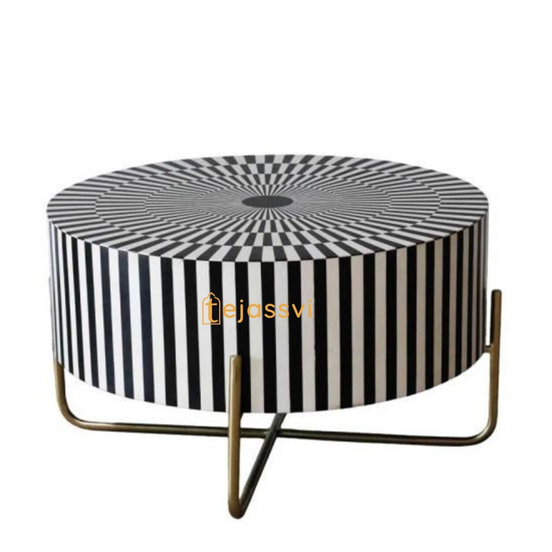 Op de afbeelding: Een ronde bijzettafel met een zwart-wit geometrisch patroon. De bovenkant heeft een concentrisch vierkant patroon, terwijl de zijkanten verticale strepen vertonen. Hij wordt ondersteund door een goudkleurige metalen voet.