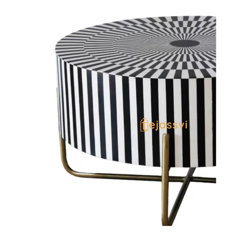 Op de afbeelding: Een ronde bijzettafel met een zwart-wit geometrisch patroon. Het tafelblad heeft een concentrisch cirkelontwerp, terwijl de zijkanten verticale strepen hebben. De tafel wordt ondersteund door goudkleurige metalen poten.
